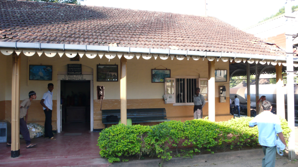 Alt 1: Peradeniya Railway Station platform with trains and green hills in the background